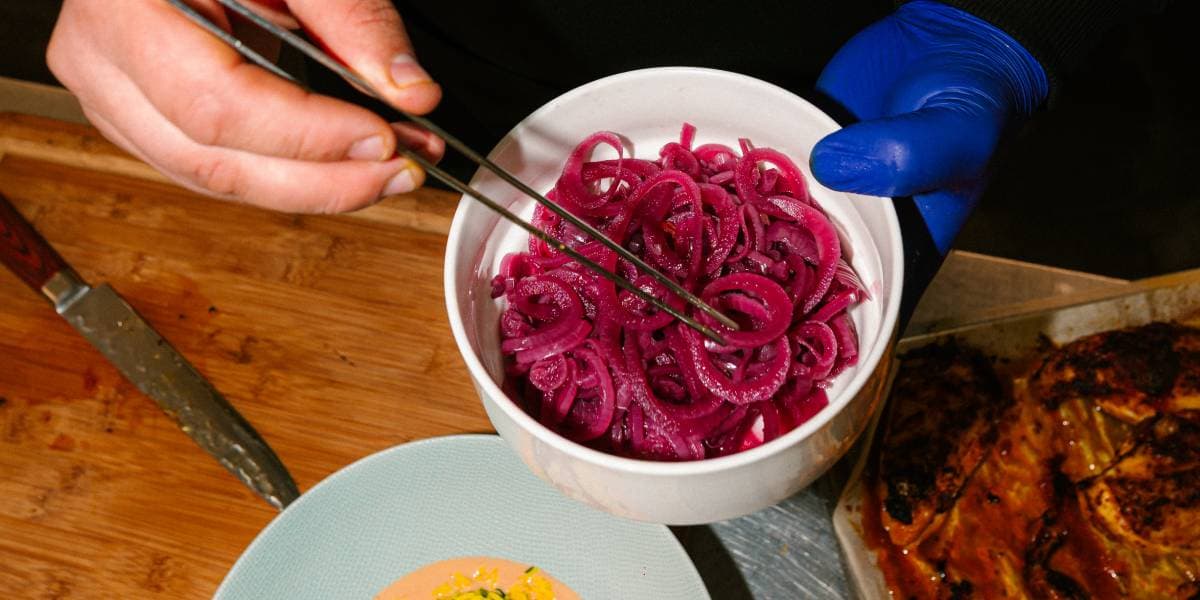 En cuisine, des oignons rouges marinés dressés à la pince